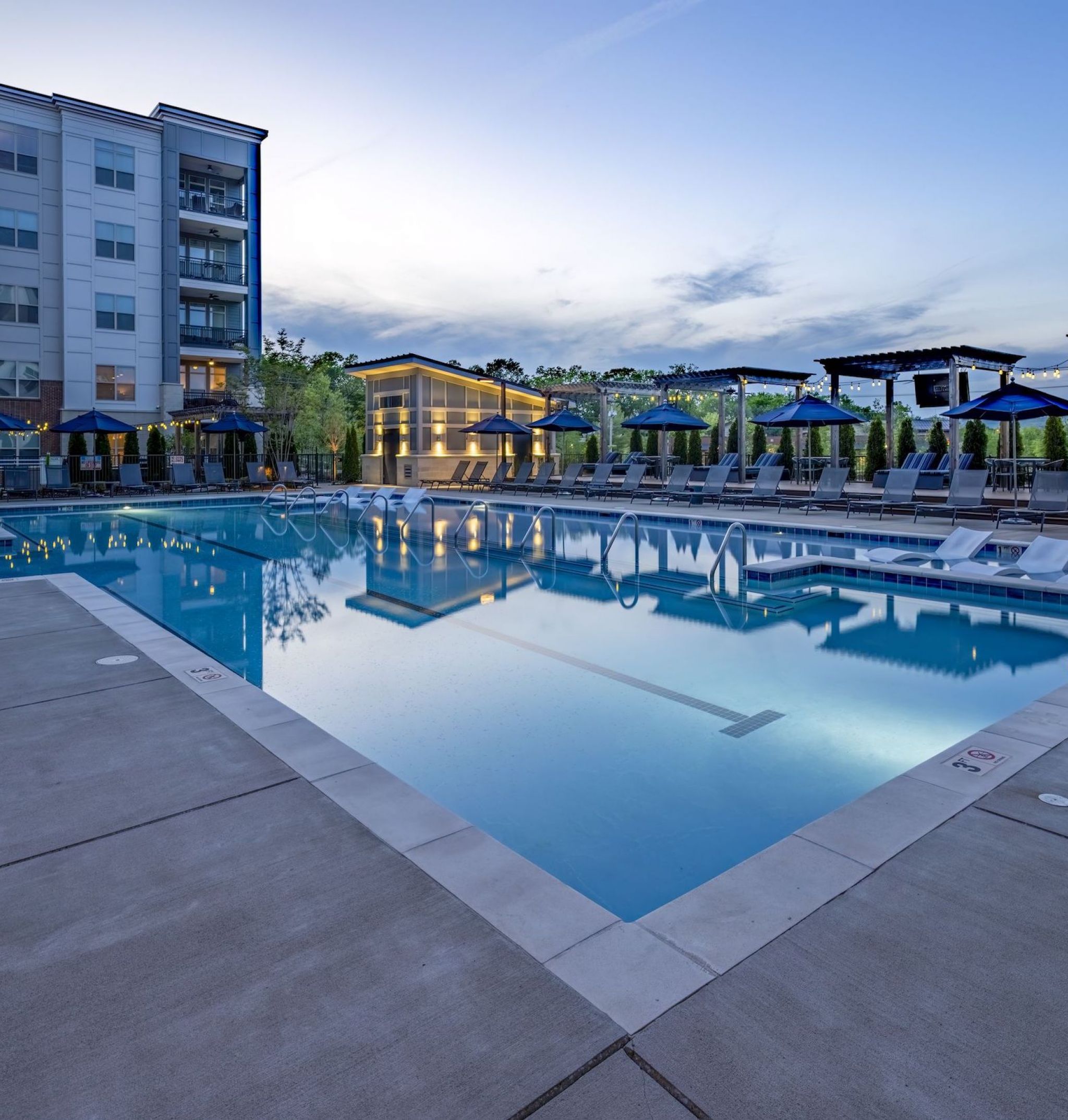 Beautiful view of McEwen Northside Apartment's luxury outdoor pool at night with seating and umbrellas