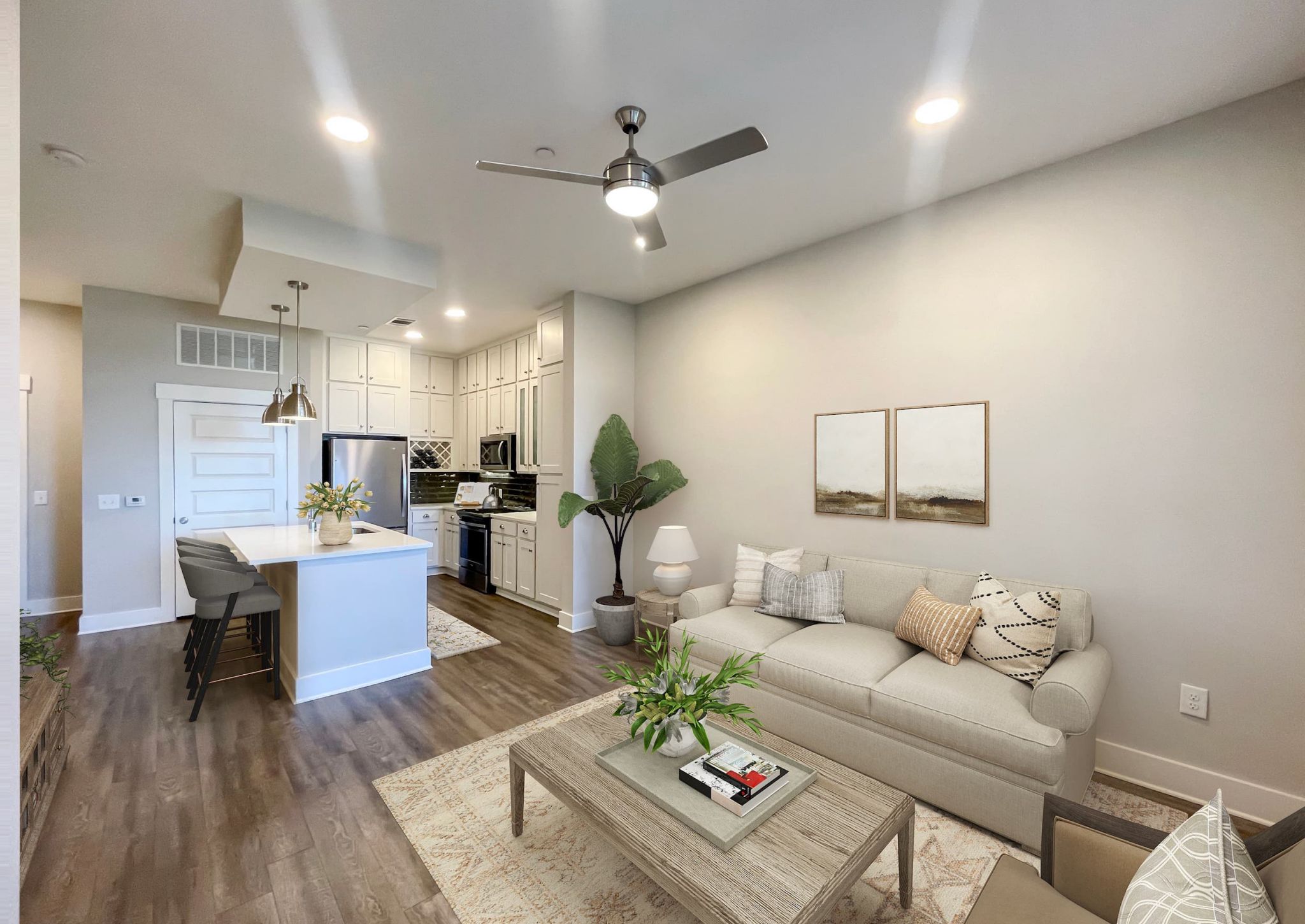 Open concept apartment showing living area with couch, coffee table, and chair and kitchen area with kitchen island and lots of cabinet storage